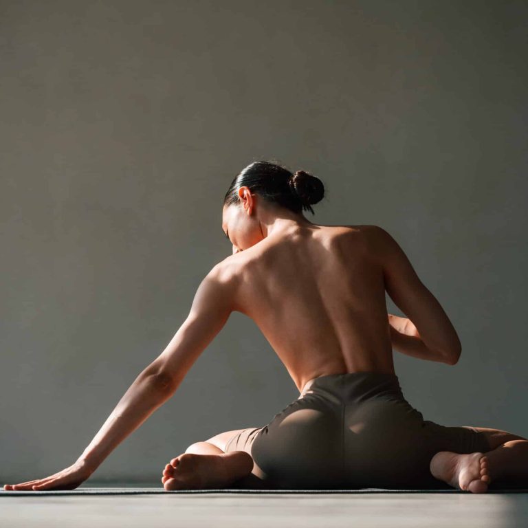 Without bra, sitting on the floor. Young woman with slim body type is in fitness clothes in the studio.